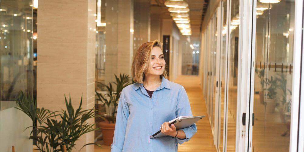 uśmiechnięta dziewczyna z laptopem w ręce na korytarzu w biurze; opinia kamili